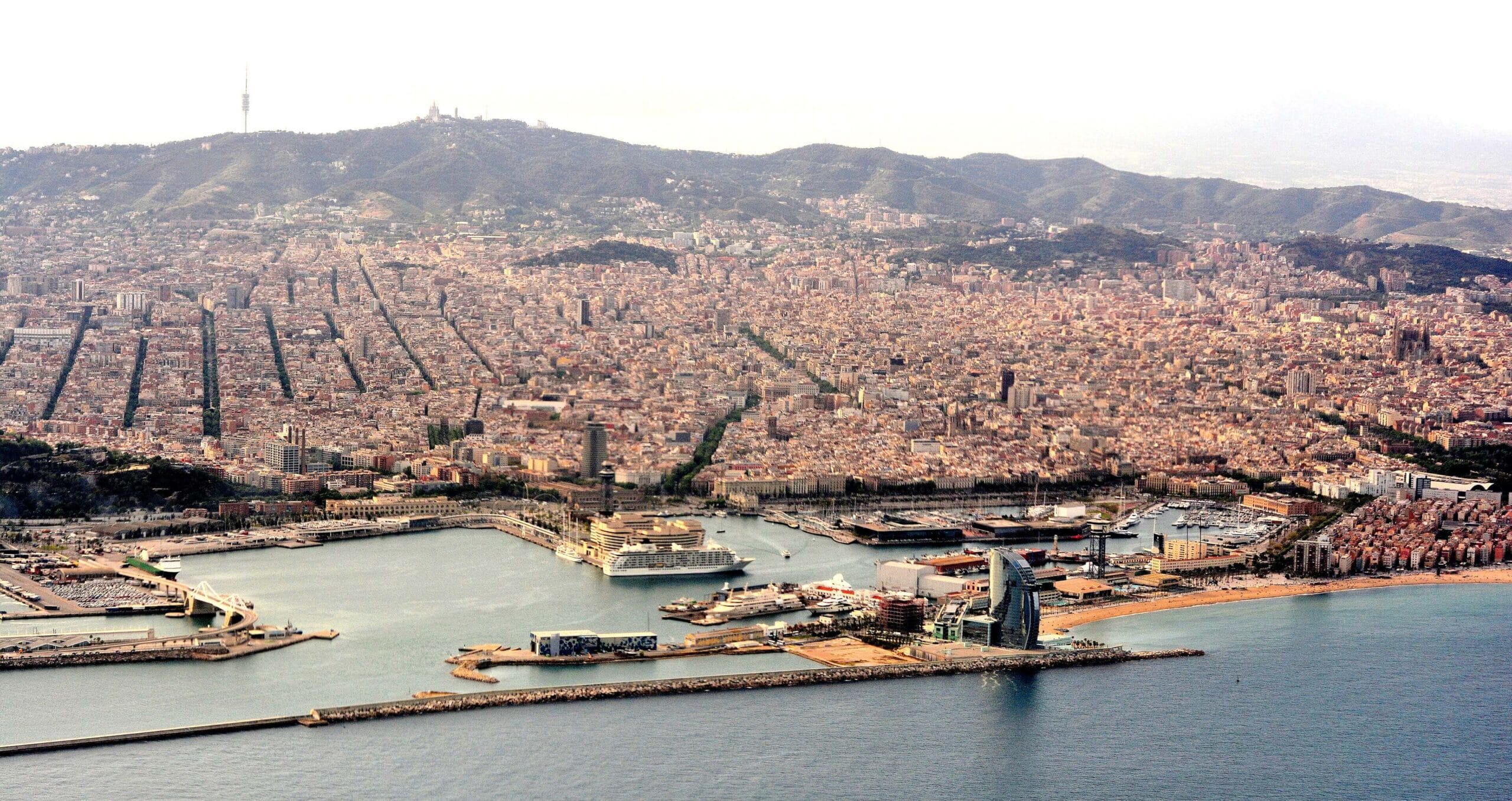 Vista panorámica de Barcelona al atardecer, con el puerto, la Sagrada Familia y la montaña de Tibidabo al fondo.