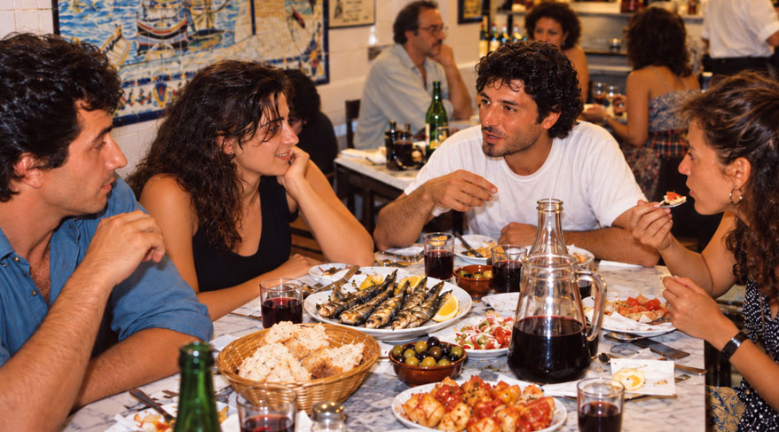 Personas disfrutando de una comida en un bar tradicional de Barcelona, con platos de cocina catalana sobre la mesa.