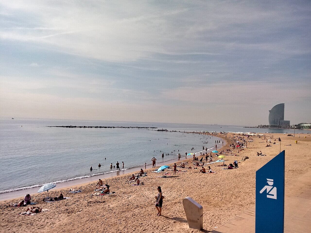 Playa de la Barceloneta con arena, mar y paseo marítimo con edificios urbanos al fondo en un día soleado